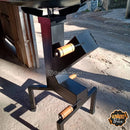 Churrasqueira preta com estrutura metálica e alças de madeira em ambiente externo ao ar livre