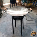 Fogão a gás com chapa metálica marmorizada em formato flor, com pega de madeira, em ambiente de oficina