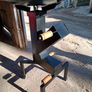 Suporte metálico preto para moedor com alças de madeira, em chão de cimento exposto à luz do sol