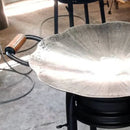 Grelha redonda em metal com borda ondulada e alça com detalhe em cobre, ambiente de cozinha industrial