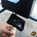 Mão segurando alça de madeira preta, componente de equipamento metálico em fundo de chão de terra