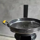 Panela de ferro fundido com alça amarela sobre fogão preto em ambiente cinza