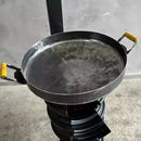 Chapa de ferro com alças amarelas sobre fogareiro portátil preto em fundo cinza