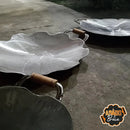 Funil de chapa com alças de madeira, dois modelos grandes em formato ondulado, sobre chão rústico