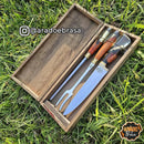Conjunto de faca, garfo e chaira com cabo de madeira em caixa artesanal sobre grama verde